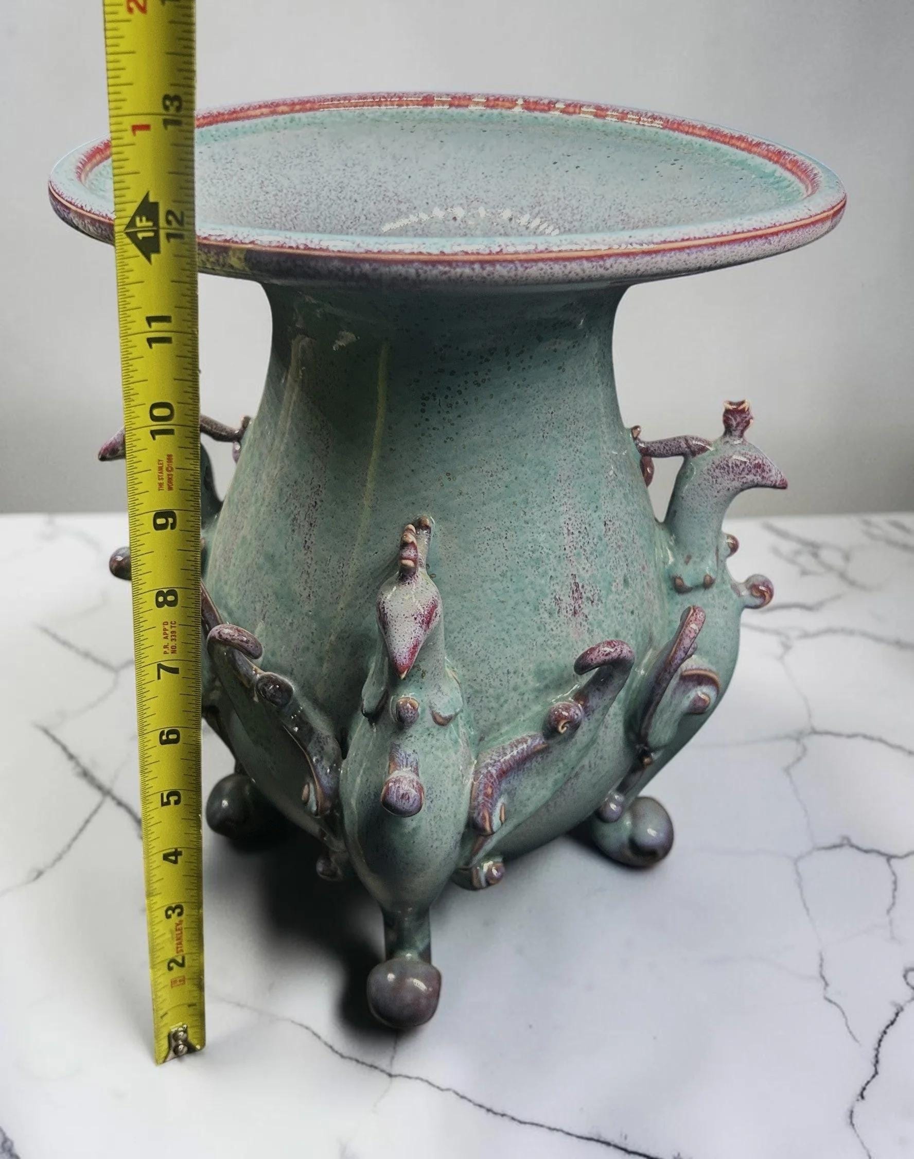 C&C Atelier celadon ceramic pedestal vase with purple accents and sculpted bird motifs on a tripod base.