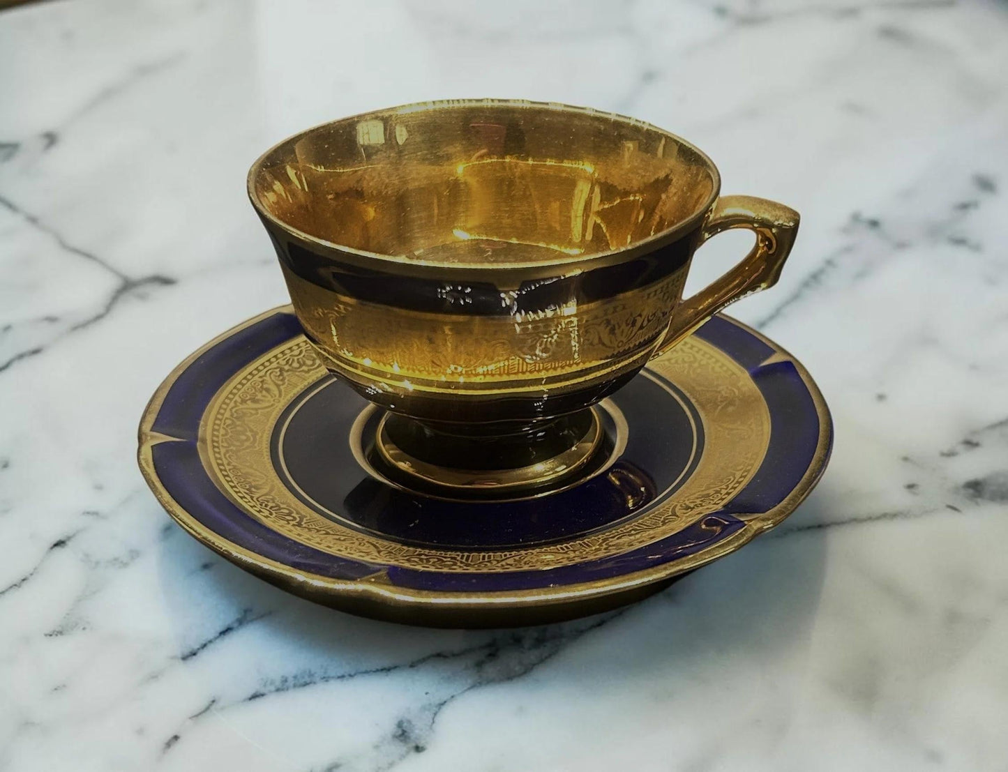 C&C Atelier gilded porcelain teacup and saucer, deep cobalt blue with intricate gold detailing and embossed pattern.